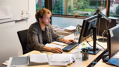 Businessman working at a desk on their computer surrounded by paperwork.