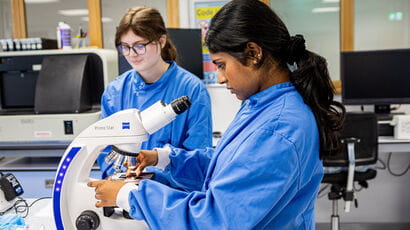 A young adult using a microscope in a lab environment.