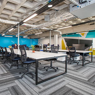 Room with large white co-working desks and exposed concrete ceiling.