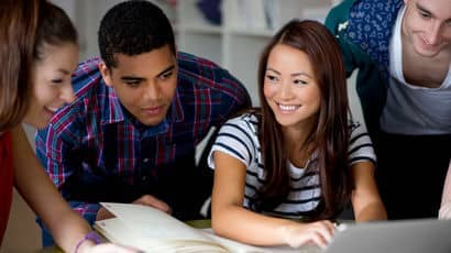 Four students happily looking at a laptop together.