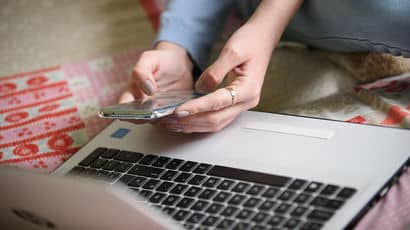 Hands holding a mobile phone in front of a laptop.