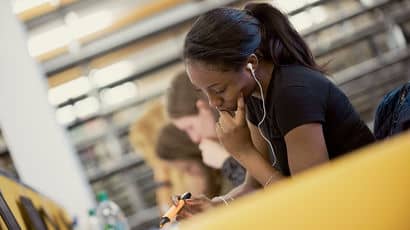 A student wearing earbuds works on a laptop.