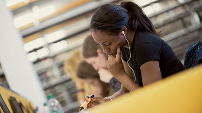 A student wearing earbuds works on a laptop.