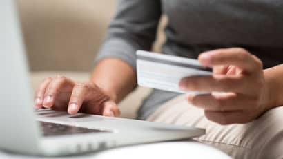 Close up of a hand holding a credit card in front of a laptop