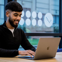 A student smiling whilst working on a laptop