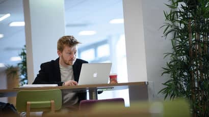 A visitor is sitting at a table and working on a laptop in Onezone at Frenchay Campus.