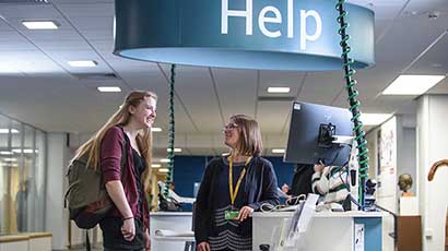 Student approaching a member of staff behind a helpdesk