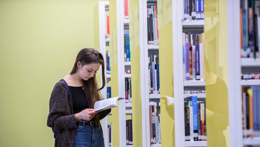 Student reading next to bookshelves in Glenside Library.