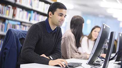 A student using a computer in the library to check database service interruptions.