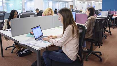 Student working at laptop with paperwork on desk.