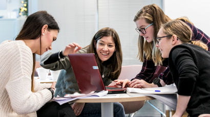 Four students working at a table, three looking at a laptop