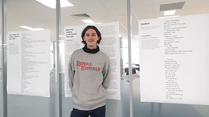 Lewis Williams, Writer in Residence standing in front of his poems on display.