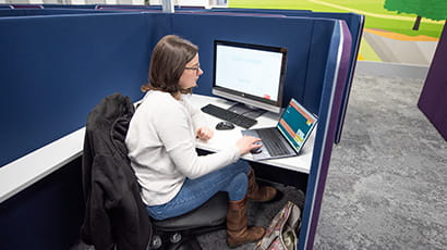 student working on desktop computer and laptop in silent study booth