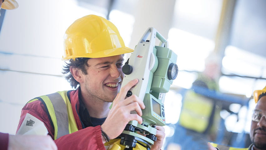 A student in protective gear surveying construction site alongside other students