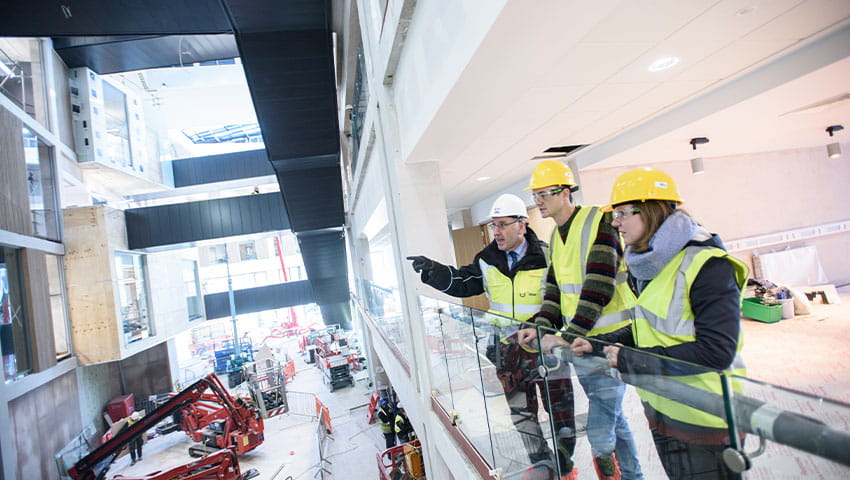 An instructor lecturing two students inside a building that is under construction