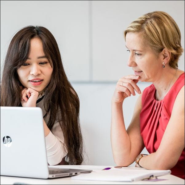 Student and staff member having a conversation in front of a laptop.