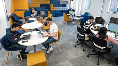 Wide shot of group study space with students working on laptops and computers
