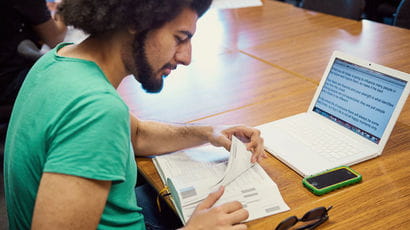 Student reading while using a notebook computer in a study space.