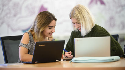 Two students having a conversation while using laptops.