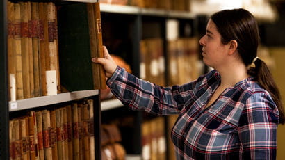 Student reaching for a book on a shelf.