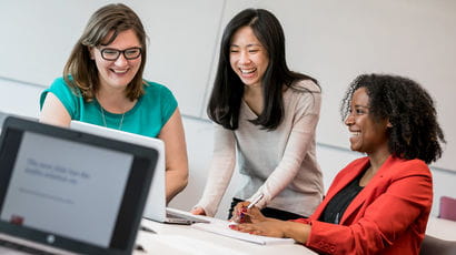 Three female students gathered around a laptop