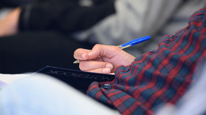 Closeup of someone sitting in a lecture with a pen and paper.
