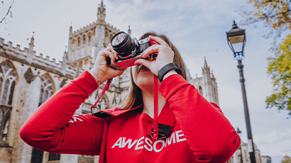 A girl in a red hoodie that says 'awesome' taking a photograph of the city