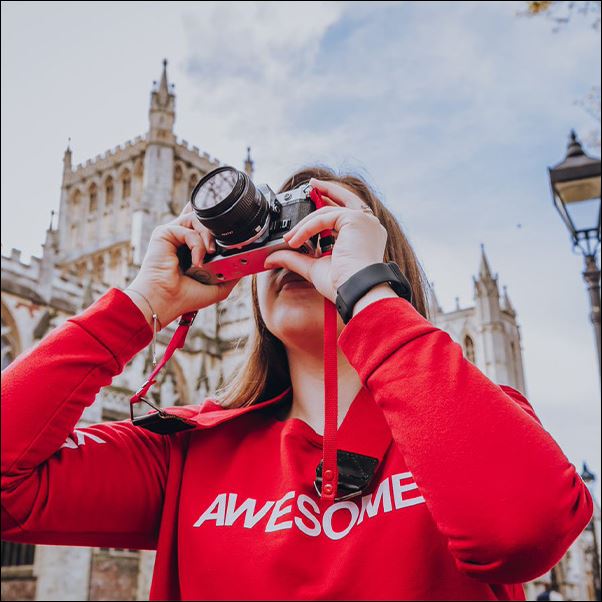 A girl in a red hoodie that says 'awesome' taking a photograph of the city