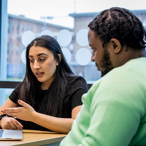 Man in bright green sweater looking to woman talking and referring to laptop screen.
