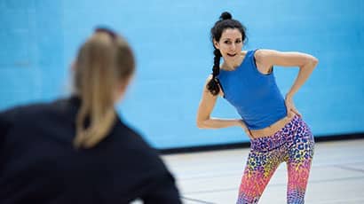 An instructor demonstrates a move with rotating with hands on hips in the Sports Hall. 