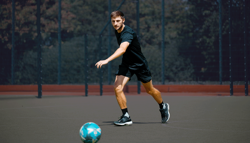 Man in black sports clothes preparing to kick a football on an outdoor football pitch.