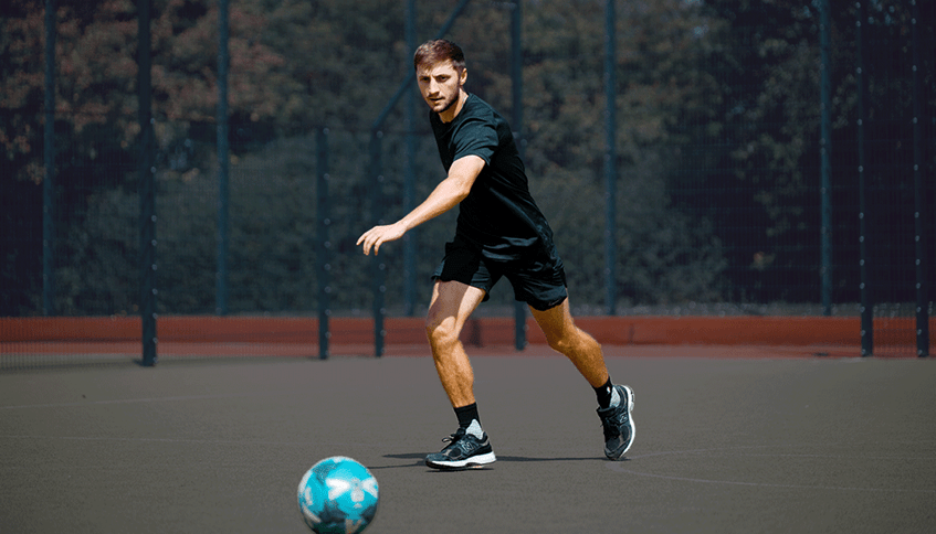Man in black sports clothes preparing to kick a football on an outdoor football pitch.