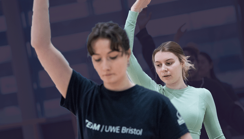 People in an exercise studio holding arms overhead in a pose.