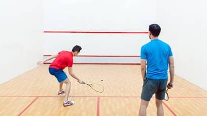Two men with their backs to camera playing squash in a squash court.