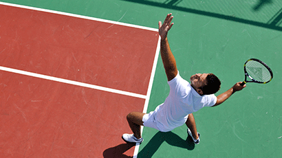 Overhead view of a man in tennis whites throwing a ball up for overhead serve.
