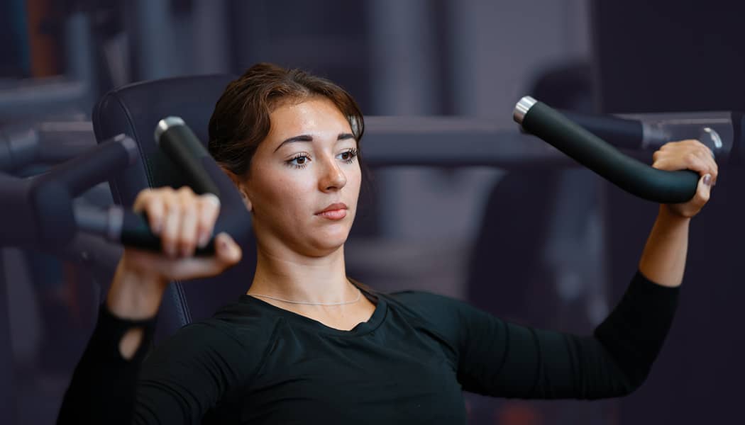 A woman holding handlebars of a shoulder press machine in the gym.