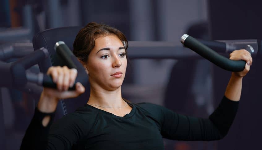 A woman holding handlebars of a shoulder press machine in the gym.