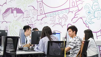 Students sat together looking at monitors in front of a wall with a modern sketch of Bristol on.