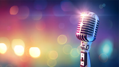 An old-fashioned microphone gleaming in the spotlight with colourful lights in the background.