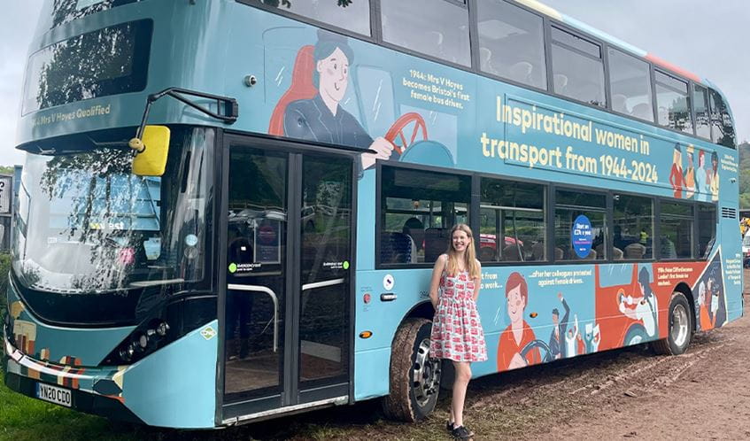 UWE Bristol illustration student Rosalyn Burroughs stands in front of a double decker bus featuring her winning design 
