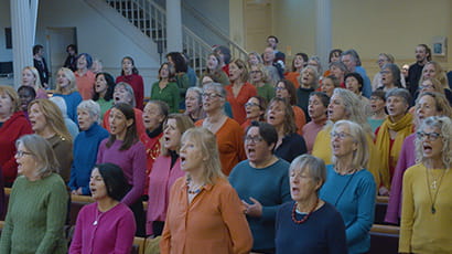 A group of people are enthusiastically singing, while wearing brightly coloured jumpers.